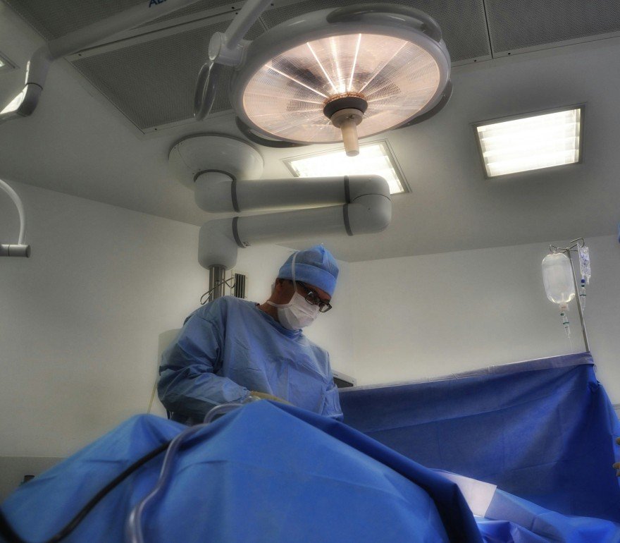Surgeon in blue surgical attire performing a procedure in an operating room.