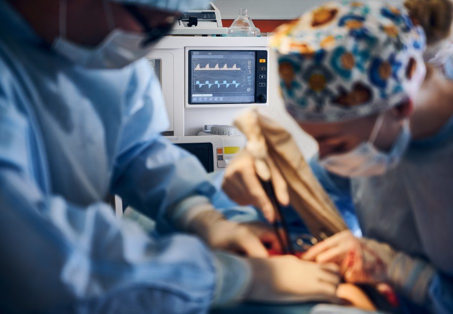 Surgeons performing Fissure Surgery in an operating room with a patient monitor visible in the background.