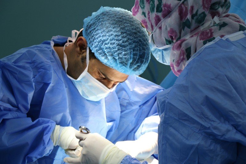 Laparoscopic Surgeon performing a surgical procedure in an operating room while wearing sterile gloves, a surgical mask, and protective clothing